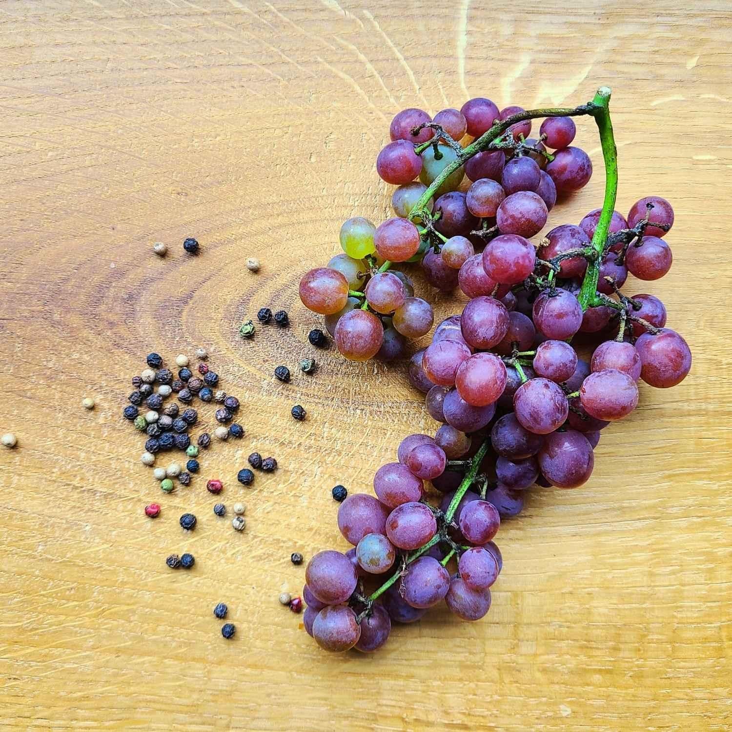Trauben und Pfefferkörner auf Holztisch Naturstoff