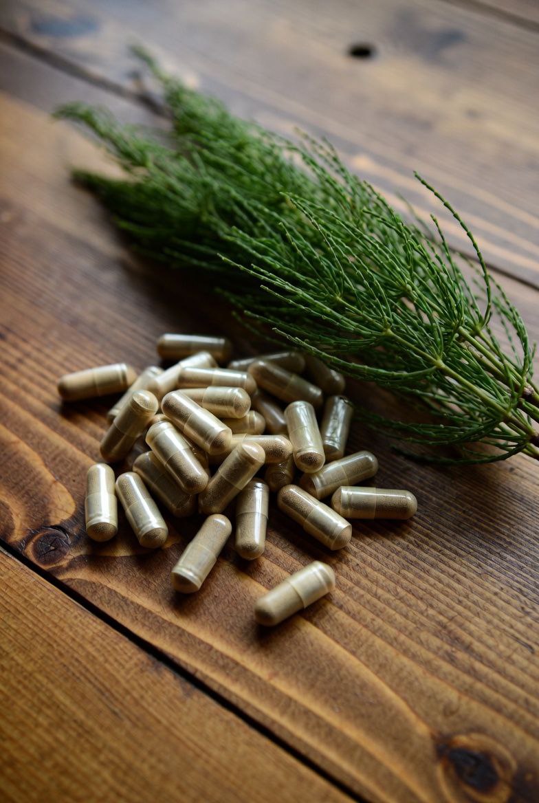 Spurenelemente Kapseln mit Ackerschachtelhalm auf Holztisch von Naturstoff